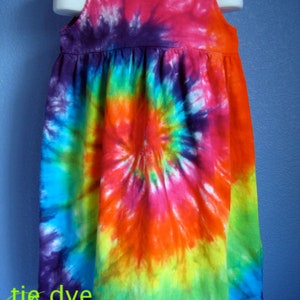 May include: A colorful tie-dye dress with a spiral pattern in shades of blue, green, yellow, orange, pink, and purple. The dress has a sleeveless design and a scoop neckline.