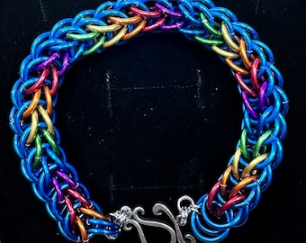 May include: A rainbow colored metal chain bracelet with a silver clasp. The bracelet is made of small, interlocking rings.