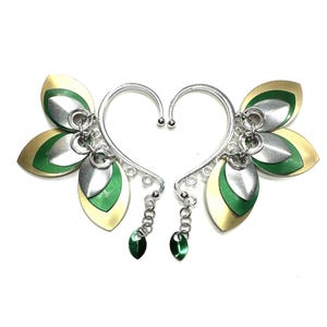May include: A pair of silver ear cuffs with green and gold leaf-shaped charms. The cuffs are designed to wrap around the ear and have a dangling charm at the bottom.