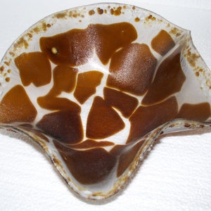 May include: A white glass bowl with a brown, abstract, giraffe-like pattern. The bowl has a wavy, organic shape.
