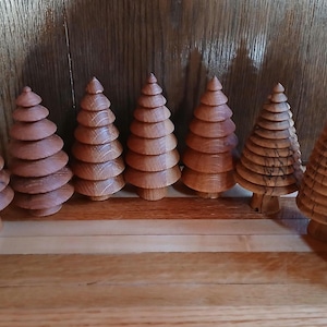 May include: A set of ten wooden Christmas tree ornaments, each with a unique wood grain pattern and a layered design. The ornaments are arranged in a row on a wooden surface.