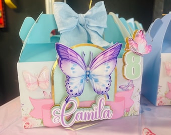 May include: Light blue party favor box with a large purple and blue butterfly decoration. The box features a pink banner with the name "Camila" and a number "8". A light blue bow adorns the top of the box, with additional butterfly accents.
