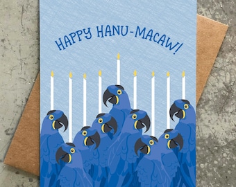 Puede incluir: Una tarjeta azul con el texto "Happy Hanu-Macaw!" y una menorá hecha de guacamayos azules con velas amarillas.