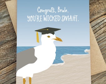 May include: A graduation card with a seagull wearing a graduation cap. The card has a blue sky and ocean background with a sandy beach. The text on the card reads "Congrats, Bruh. You're Wicked Smaht."