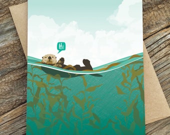 May include: A greeting card featuring a cartoon illustration of a sea otter floating on its back in a bed of kelp. The otter is smiling and has a speech bubble above its head that says "Hi".