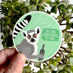 May include: A round sticker with a cartoon lemur holding a bottle of wine. The lemur has a speech bubble that says "I'm fine. Everything is fine."