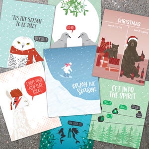 May include: A collection of humorous holiday greeting cards with various designs. One card features an owl in a scarf, another a bear with wine bottles, and others with quirky illustrations and text like "Enjoy the Season."