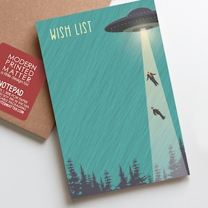 May include: A notepad with the words "WISH LIST" and an illustration of a UFO beaming up two people. The notepad has a teal background with a forest silhouette at the bottom. A red sticker on the side reads "MODERN PRINTED MATTER".