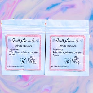 May include: Two small white pouches with pink labels that read "Crabby Corner Co. Hibiscus Calcium". The labels also list the ingredients: "Dried Hibiscus, Lobster & Crab Shell Powder". The pouches have a pink and white hibiscus flower and a red lobster illustration on the front. The text "NOT FOR HUMAN CONSUMPTION" is printed on the bottom of each label.