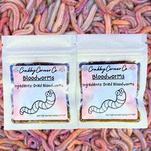 May include: Two white resealable bags with labels that say "Crabby Corner Co. Bloodworms" and "Ingredients: Dried Bloodworms". The bags are filled with dried bloodworms. The labels also have a cartoon bloodworm with the text "Not for human consumption".