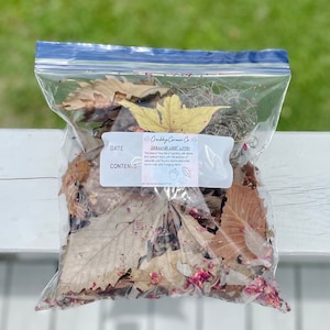 May include: A clear plastic bag filled with a variety of dried leaves and petals. The bag has a label that reads "Crafty Corner Co. Seasonal Leaf Litter. The bulk of this mix is typically with leaves and sprouted moss with the addition of other natural elements like acorns, berries and other items that are safe for crafting. Not for human consumption."