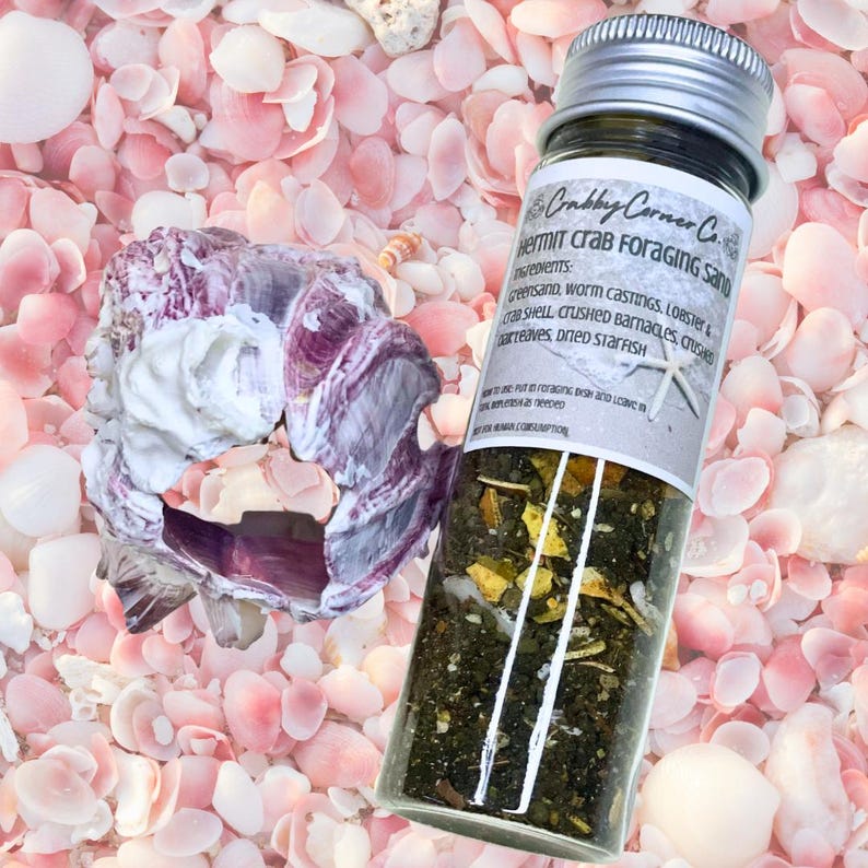 May include: A clear glass jar with a silver screw-top lid containing Crabby Corner Co. hermit crab foraging sand. The label lists ingredients including greensand, worm castings, lobster and crab shell, crushed barnacles, and dried starfish.