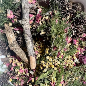 May include: A bowl filled with dried flowers, herbs, and twigs. The mixture includes pink rose petals, yellow chamomile flowers, green sprigs, and brown twigs.