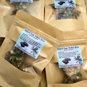 May include: Four brown paper pouches containing Hermit Crab Protein Bars. Each label features an octopus graphic, the text Hermit Crab Protein Bars, ingredients list, and crabbycornerco.etsy.com. The contents are visible through a clear window.