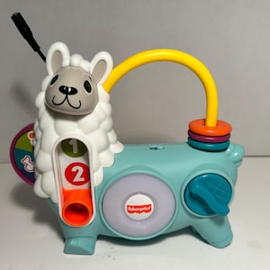 May include: A Fisher-Price llama-shaped toy in light blue, white, and gray. It features a yellow handle, colorful rings, and a dial. The toy has the numbers 1 and 2, and a Fisher-Price logo.