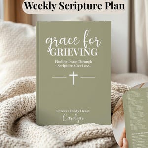 May include: A sage green journal titled Grace for Grieving: Finding Peace Through Scripture After Loss, featuring a white cross icon and the text Forever In My Heart Carolyn. A smaller inset shows the back cover with a weekly scripture plan list.
