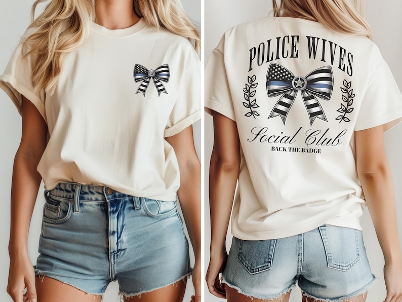 Puede incluir: Camiseta color crema con un dise&ntilde;o de lazo con la bandera estadounidense y una l&iacute;nea azul. La parte trasera de la camiseta muestra el texto "POLICE WIVES Social Club" y "BACK THE BADGE" con un gr&aacute;fico de lazo similar y hojas de laurel.