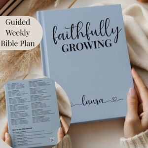 May include: A pale blue journal with the words "faithfully GROWING" in black script. The name "laura" is written below, with a heart symbol. The journal is open to a page with text.