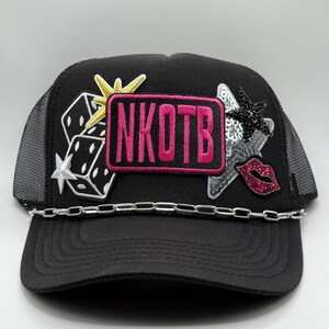 May include: Black trucker hat with a silver chain and patches. The patches include dice, stars, and a pink rectangle with the letters "NKOTB". A sequined star and a pink sequined lip patch are also present.