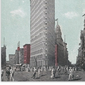 Puede incluir: Una postal vintage que representa el Flatiron Building en la ciudad de Nueva York. El edificio es un rascacielos triangular distintivo con una fachada gris claro y una base de ladrillo rojo. La postal muestra el edificio desde una perspectiva a nivel de calle, con personas caminando por la acera frente a él.