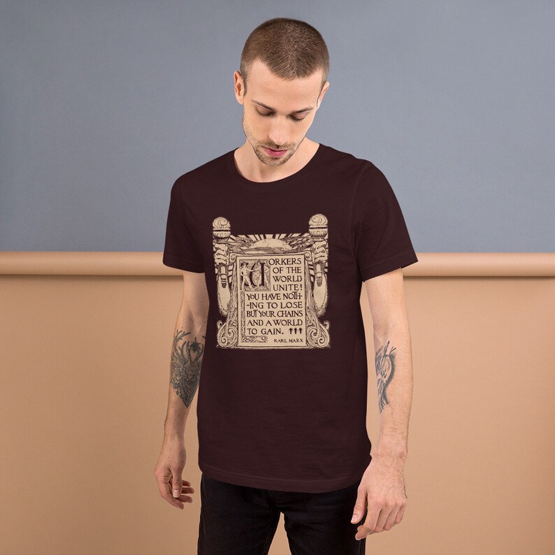 Puede incluir: Una camiseta marr&oacute;n con un estampado gr&aacute;fico vintage de una cita de Karl Marx. La cita dice: "&iexcl;Trabajadores del mundo, un&iacute;os! No ten&eacute;is nada que perder m&aacute;s que vuestras cadenas y un mundo que ganar."