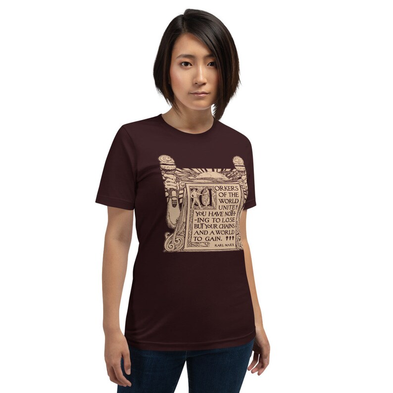 Puede incluir: Una camiseta marr&oacute;n con un estampado gr&aacute;fico de estilo vintage de un rollo con el texto "Trabajadores del mundo, &iexcl;un&iacute;os! No ten&eacute;is nada que perder m&aacute;s que vuestras cadenas y un mundo que ganar." El texto se atribuye a Karl Marx.