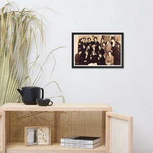 May include: A black and white photo of a group of people, mostly women, posing for a photo. They are all dressed in formal attire, and some are wearing hats. The photo is framed in a black frame.