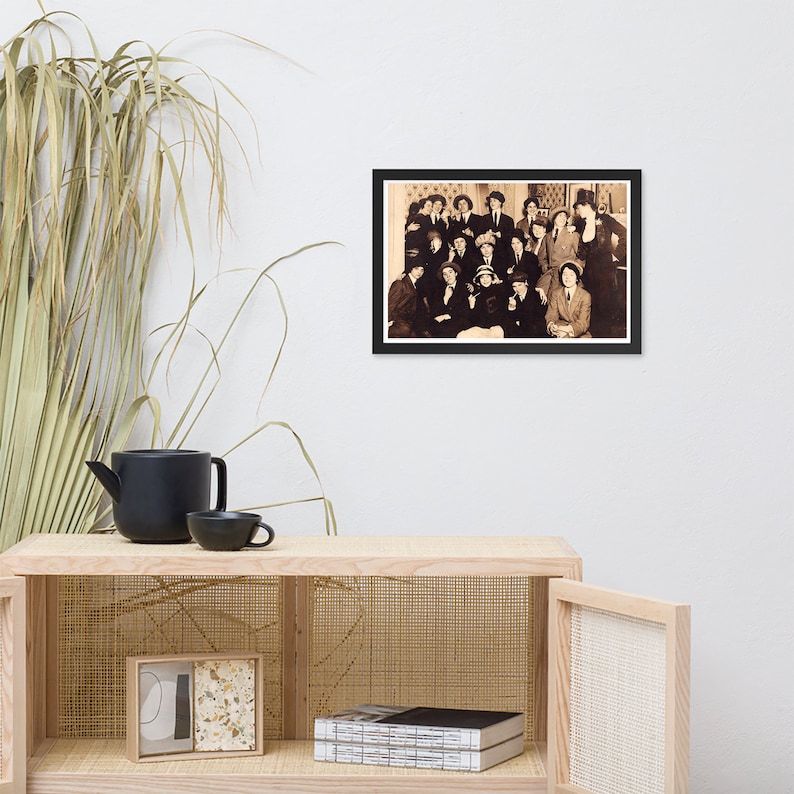 May include: A black and white photo of a group of people, mostly women, posing for a photo. They are all dressed in formal attire, and some are wearing hats. The photo is framed in a black frame.