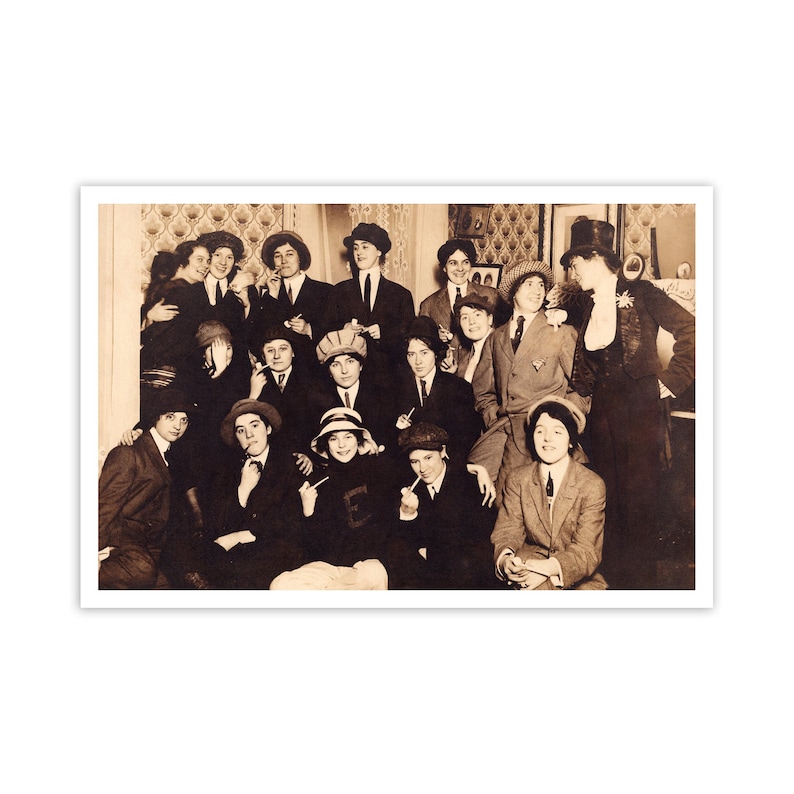 May include: A black and white vintage photograph of a group of people, mostly women, posing for a photo. They are all dressed in formal attire and some are wearing hats. The photo appears to have been taken in a home setting.