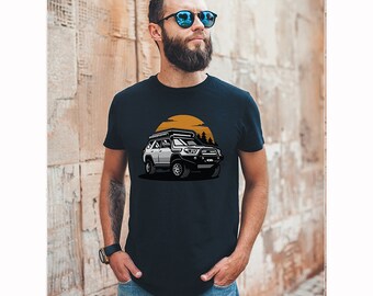 Op de afbeelding: Een marineblauw t-shirt met een witte en zwarte illustratie van een 4x4-voertuig met een dakdrager die door een bos rijdt met een gele zonsondergang op de achtergrond.