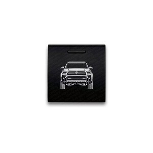 May include: A square black sign featuring a white line art illustration of a Toyota Tacoma truck from the front view. The background is patterned with the repeating text CHX4 INDUSTRIES. The truck design includes a grille, headlights, and a light bar.