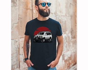 Könnte beinhalten: Marineblaues T-Shirt mit einer Grafik eines weißen SUV vor rotem Sonnenhintergrund. Der SUV hat schwarze Reifen und eine Frontstoßstange. Das T-Shirt besteht aus einem weichen Material.