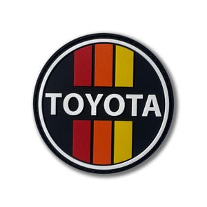 May include: A black and white circular patch with the word "TOYOTA" in white letters. The patch has a red, orange, and yellow striped design in the center.
