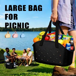 Puede incluir: Una bolsa de picnic negra llena de aperitivos y fruta, sostenida por una persona. La bolsa tiene recortes en forma de coraz&oacute;n y asas negras. El texto en la imagen dice "LARGE BAG FOR PICNIC". En el fondo, un grupo hace un picnic cerca de un lago.