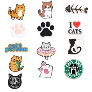 May include: A collection of cat-themed charms in various designs. Includes orange tabby cats, a fishbone, paw prints, and text that reads "I ❤️ CATS", "Cat Person", and "Crazy Cat Lads". Also features a cat in a donut and a cat-themed coffee logo.