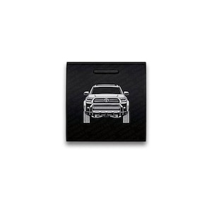 May include: A square black sign featuring a white line art illustration of a Toyota Tacoma truck front view centered on the surface. The background is patterned with repeating text that reads CH4X4 INDUSTRIES in a subtle dark grey font.