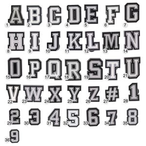 May include: A collection of black and white letter and number charms. Each charm features a bold, block letter or number design with a white center and a black border. The set includes the alphabet and numbers 1-9.