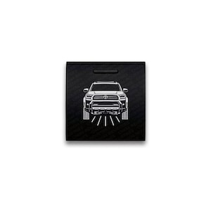 May include: A square black sticker featuring a white line art illustration of a Toyota Tacoma truck viewed from the front. The background has a repeating pattern of the text CHX4 INDUSTRIES. The truck design includes headlights, a grille, and tires.