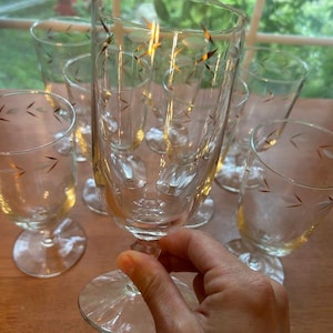 May include: A set of clear glass goblets with gold leaf accents. The goblets have a delicate design and are arranged on a wooden surface. The stemware is ideal for serving beverages at a formal event or special occasion.