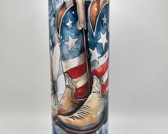 May include: A stainless steel tumbler with a patriotic design featuring cowboy boots with an American flag pattern. The boots are surrounded by blue and white flowers.