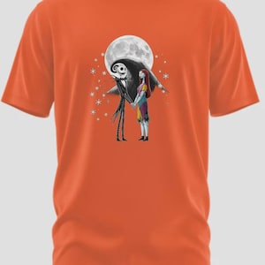 May include: Orange t-shirt featuring a graphic of Jack Skellington and Sally from The Nightmare Before Christmas, holding hands in front of a full moon. The design includes stars and is set against a black background.