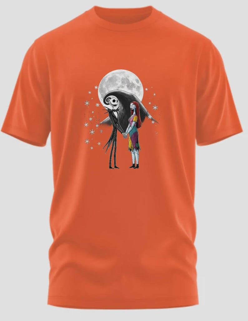 May include: Orange t-shirt featuring a graphic of Jack Skellington and Sally from The Nightmare Before Christmas, holding hands in front of a full moon. The design includes stars and is set against a black background.