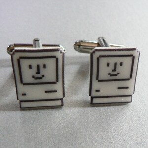 May include: A pair of silver cufflinks with a white enamel design of a vintage Macintosh computer with a smiling face.