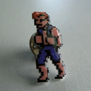 May include: A pixelated character pin with red hair, a blue shirt, and blue pants. The character is walking to the right.