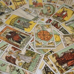 May include: A spread of tarot cards on a white surface. The cards feature colourful illustrations and text, including "The Chariot", "Strength", "The World", "The Magician", "Wheel of Fortune", "The Sun", "The Emperor", and "Temperance".