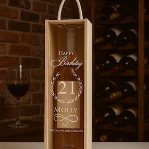 May include: A wine bottle in a wooden presentation box. The bottle is labelled with "Happy Birthday 21 Molly" and a wreath design. The box has a white handle. A wine glass is visible in the background.