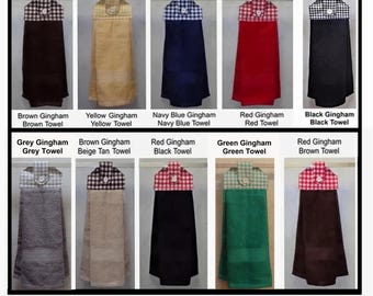 May include: A collection of hanging kitchen towels in various colors, including brown, yellow, navy blue, red, black, grey, beige, and green. Each towel features a gingham patterned top and a button closure. The text "HomeSpun LuvBy Grandma" is also visible.