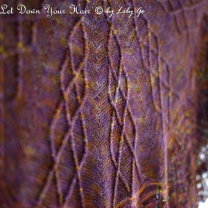 Könnte beinhalten: Nahaufnahme eines gestrickten Schals in Lila-, Braun- und Goldtönen. Der Schal hat ein Rautenmuster und einen zarten Spitzensaum. Der Text "Rapunzel, Let Down Your Hair" ist oben sichtbar.