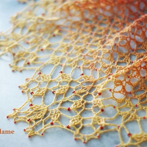 Peut inclure: Un châle crocheté avec un dégradé de couleurs orange et jaune. Le châle est décoré de petites perles rouges.