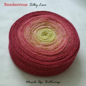 May include: A round skein of yarn with a gradient color scheme, transitioning from deep red to a pale yellow center. The yarn is labeled "Rendezvous Silky Lace" and "Muscle Up, Buttercup".